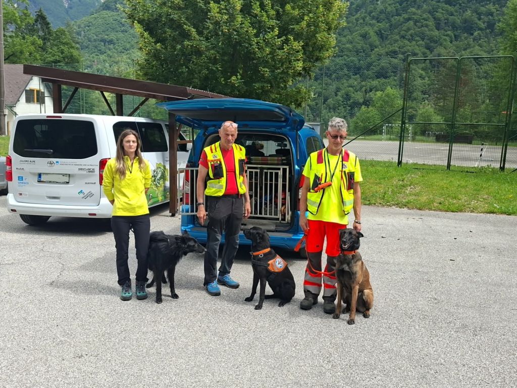 trije vodniki reševalnih psov s psi stojijo pred avtomobilom