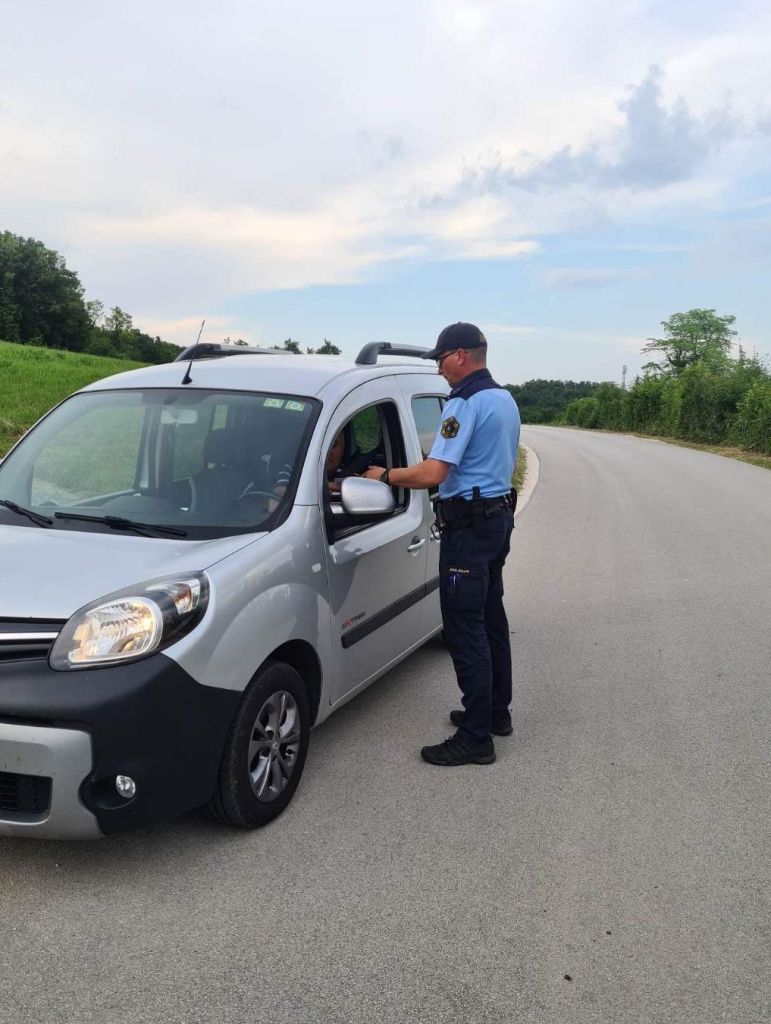Policist med kontrolo prometa - stoji ob vozilu, preverja voznikove dokumente