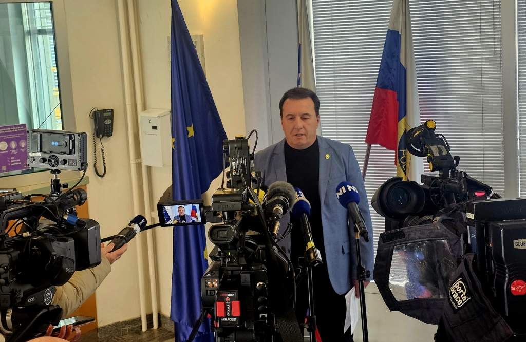 France Božičnik med izjavo za medije, stoji pred kamerami in mikrofoni, v ozadju so zastave.