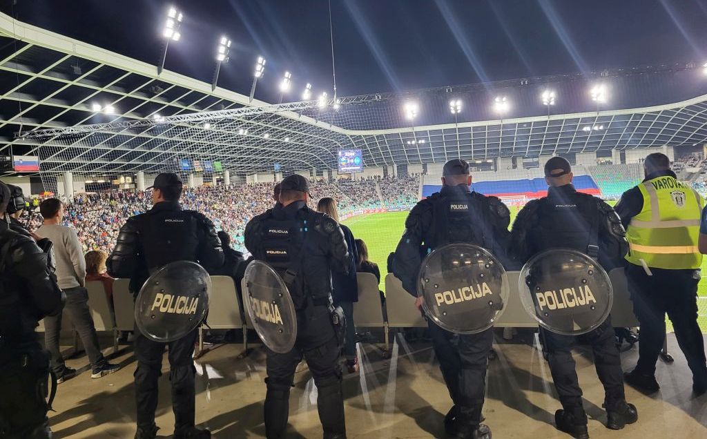 Policisti PPE stojijo ob nogometnem stadionu med tekmo, opazujejo dogajanje