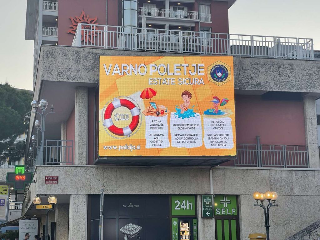 Bilingual police poster with preventive advice on the topic of Safe Summer on an electronic LED screen on the front of the house