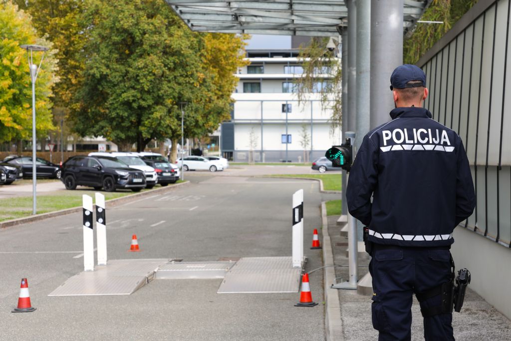 Policist, slikan "v hrbet", stoji na pločniku ob poslopju 